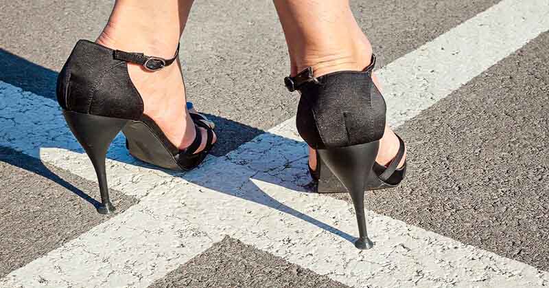 closeup of woman's feet in high heels standing on white lines going in opposite directions - illustrating a crossroads in life