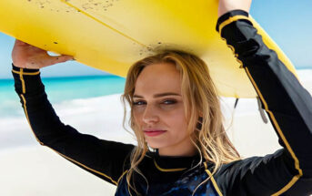 young woman in wetsuit carrying a surfboard above her head - illustrating an exciting and interesting life