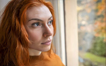 pensive young woman looking out of a window illustrating a private person