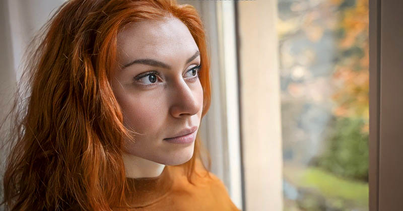 pensive young woman looking out of a window illustrating a private person