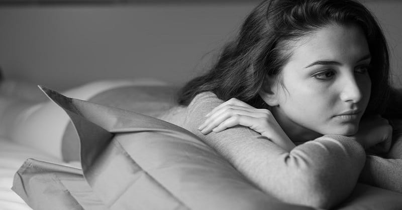 young woman lying on bed looking anxious - illustrating self-soothing techniques