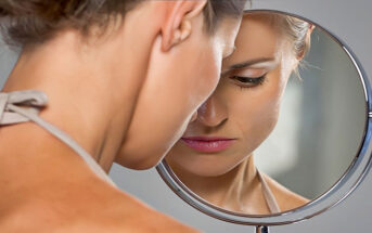 upset woman looking at herself in the mirror asking "why doesn't he want me?"