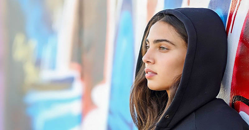 young woman leaning against a wall not knowing how she is feeling