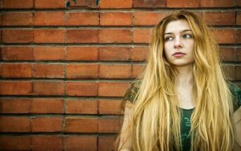 young unsatisfied woman standing in front of a brick wall