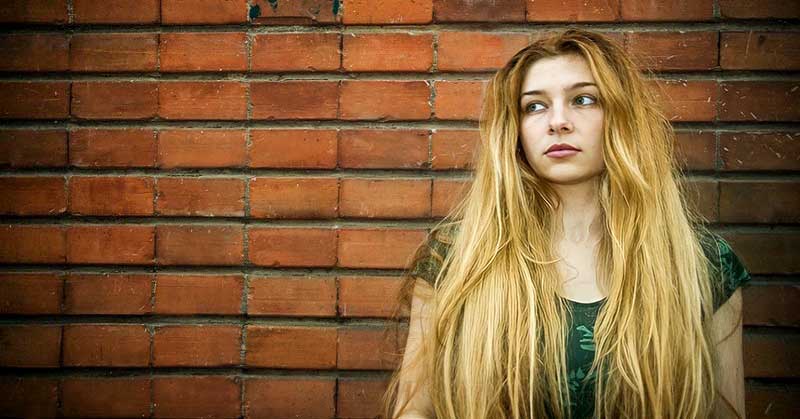 young unsatisfied woman standing in front of a brick wall