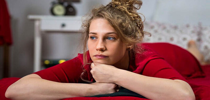 young woman looking very bored lying on her bed