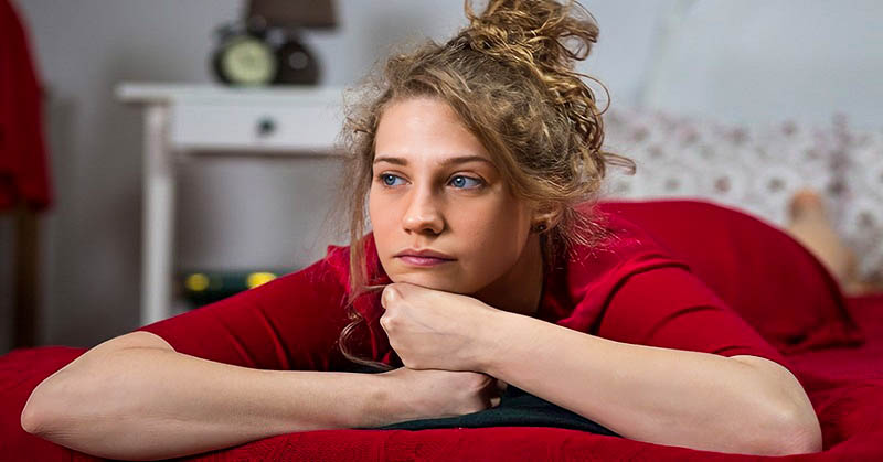 young woman looking very bored lying on her bed