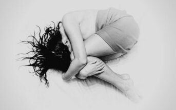 black and white photo of a young woman curled up in a ball on a bed - illustrating hopelessness