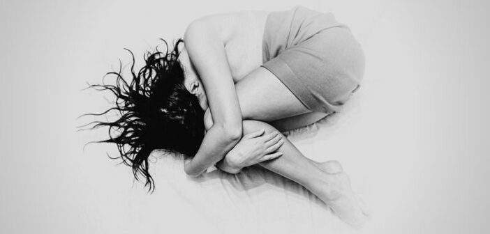 black and white photo of a young woman curled up in a ball on a bed - illustrating hopelessness