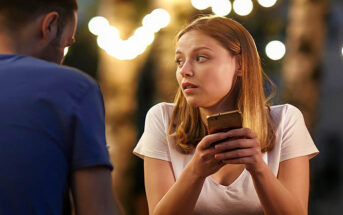 a young woman looking at her phone on a bad date - she hates dating