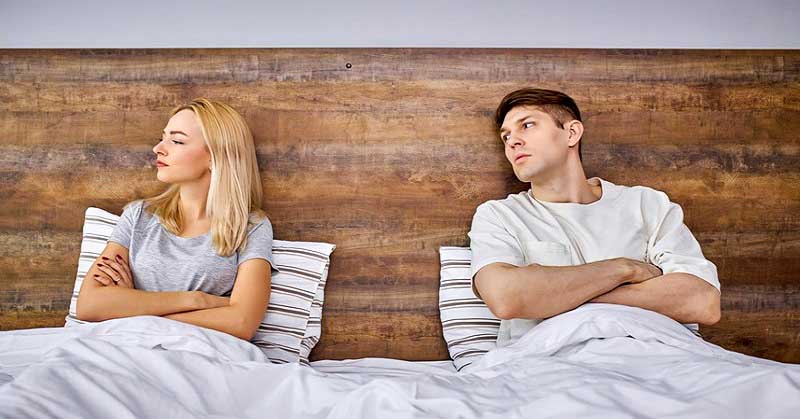 couple sitting in bed with arms crossed - illustrating a relationship with no trust