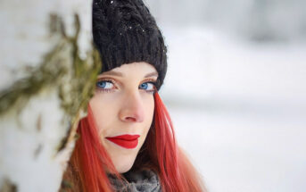 woman with red hair and red lipstick against a snowy backdrop