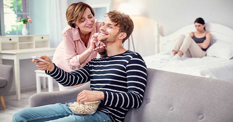 man whose mother is tending to his every need whilst girlfriend sits in the background - illustrating a mama's boy