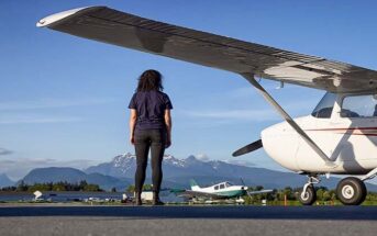 adventurous woman standing by a light aircraft with mountains in the background