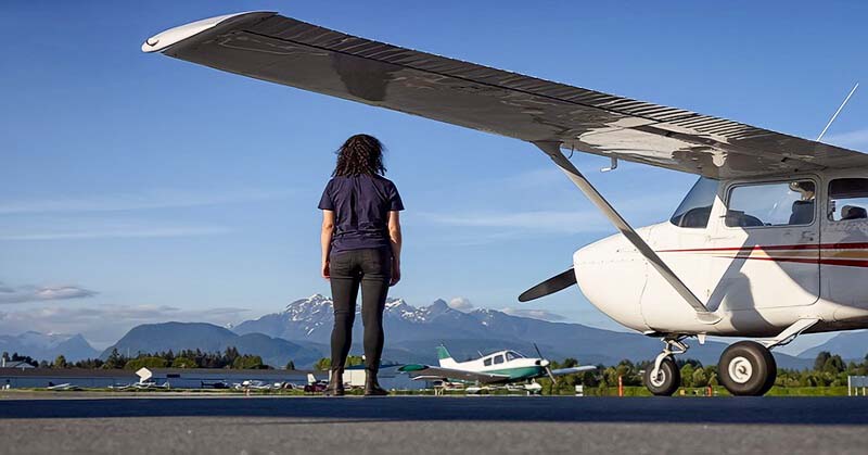 adventurous woman standing by a light aircraft with mountains in the background