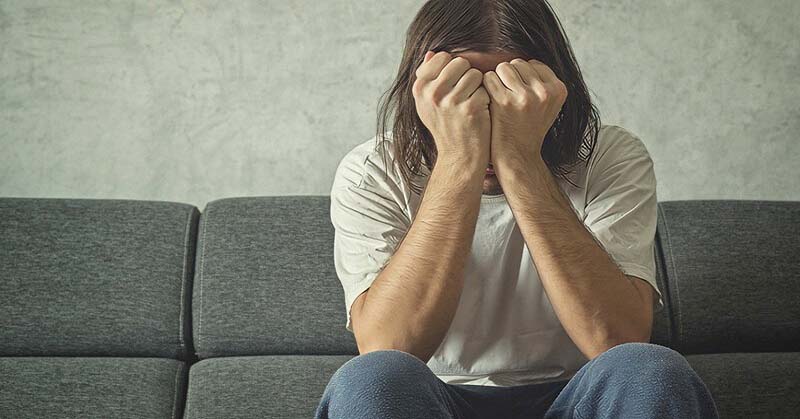 man sitting on couch with his head in his hands as his life falls apart