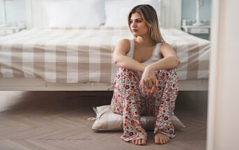 sad woman sitting on bedroom floor because her boyfriend won't commit but won't let go