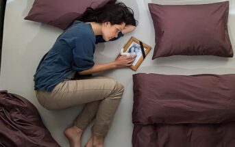 distraught woman lying on bed next to photo of her ex boyfriend - illustrating being ghosted after a serious relationship
