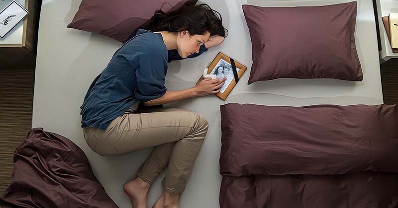 distraught woman lying on bed next to photo of her ex boyfriend - illustrating being ghosted after a serious relationship