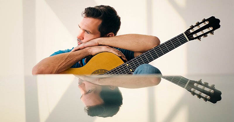 man holding guitar which he has lost interest in playing