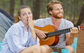 wife bored on camping trip as husband plays guitar - illustrating having nothing in common with your spouse