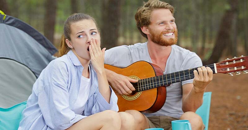 wife bored on camping trip as husband plays guitar - illustrating having nothing in common with your spouse