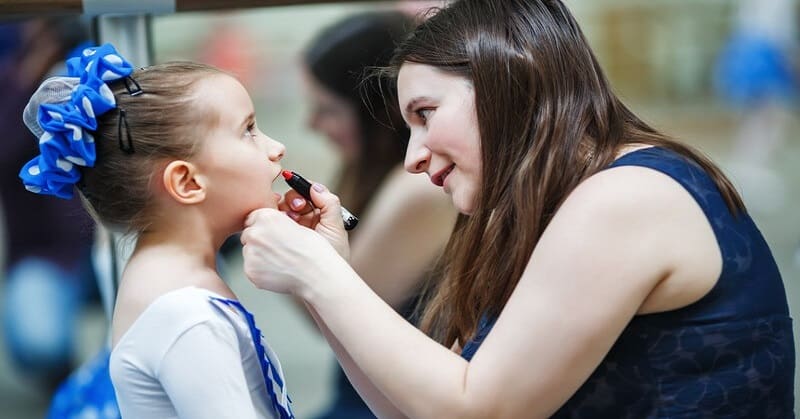 mother putting lipstick on daughter who is dressed in dance outfit - living vicariously through someone