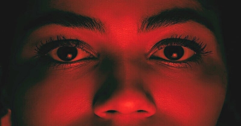 fear of being cheated on - closeup of woman's face illuminated with a red light