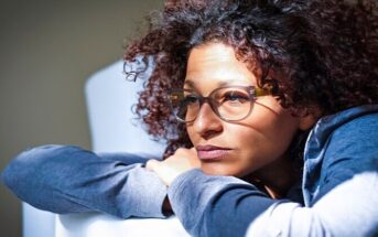 pensive woman sitting on sofa wondering if she is depressed or just lazy