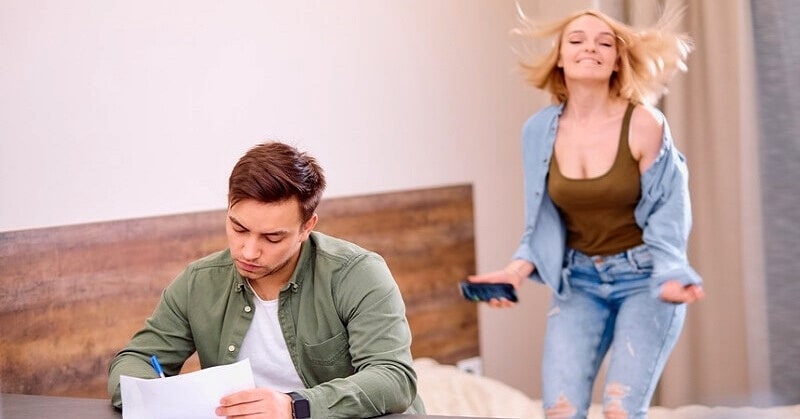 woman jumping on bed as busy man works on his desk