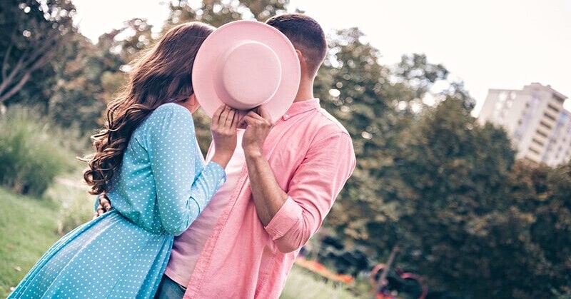 couple kissing behind hat to hide their relationship from the world