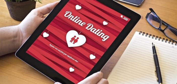 person holding tablet computer with dating website open and a writing pad next to it