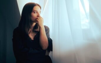 woman standing by window with gut feeling her boyfriend is cheating but no proof