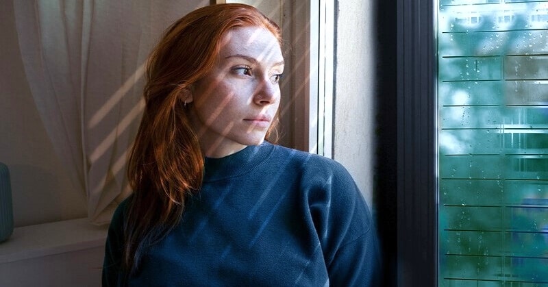 woman looking pensively out of window regretting missed opportunities