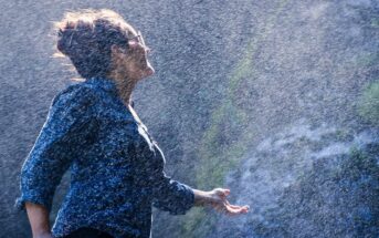 woman standing in the mist of a waterfall with her hand out