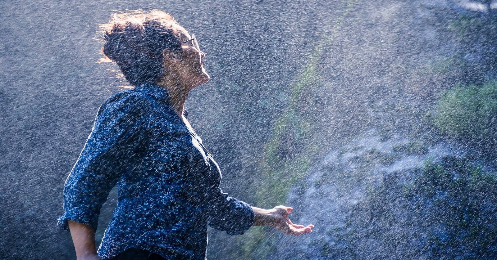 woman standing in the mist of a waterfall with her hand out