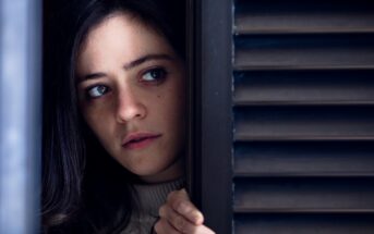 woman peeping past shutters in fear of something bad that is about to happen