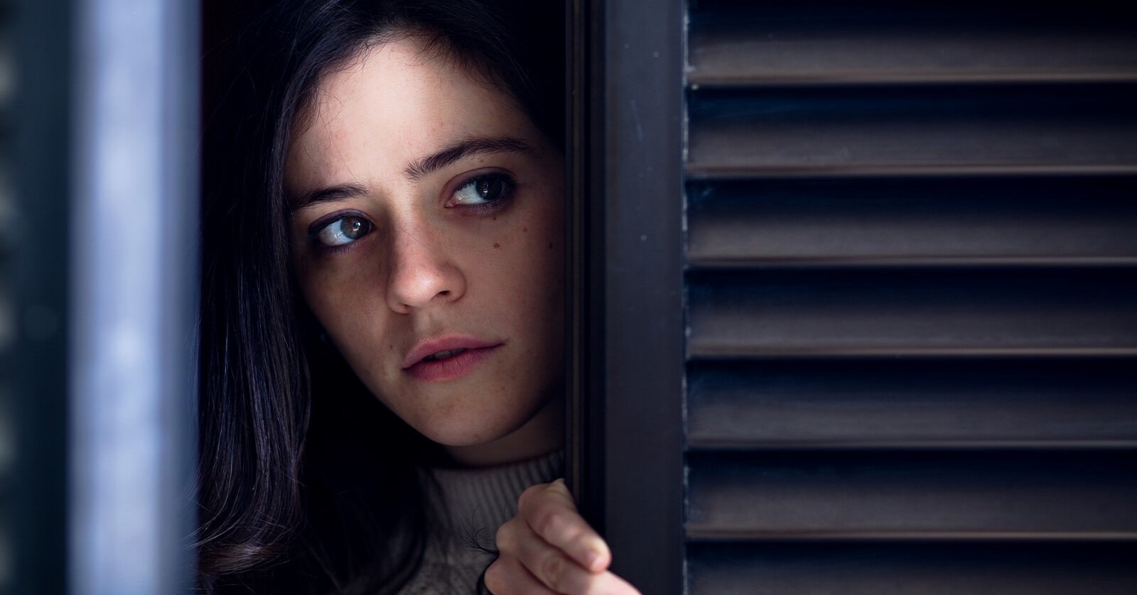 woman peeping past shutters in fear of something bad that is about to happen