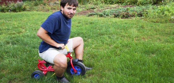 man trying to ride child's tricycle who needs to stop being childish