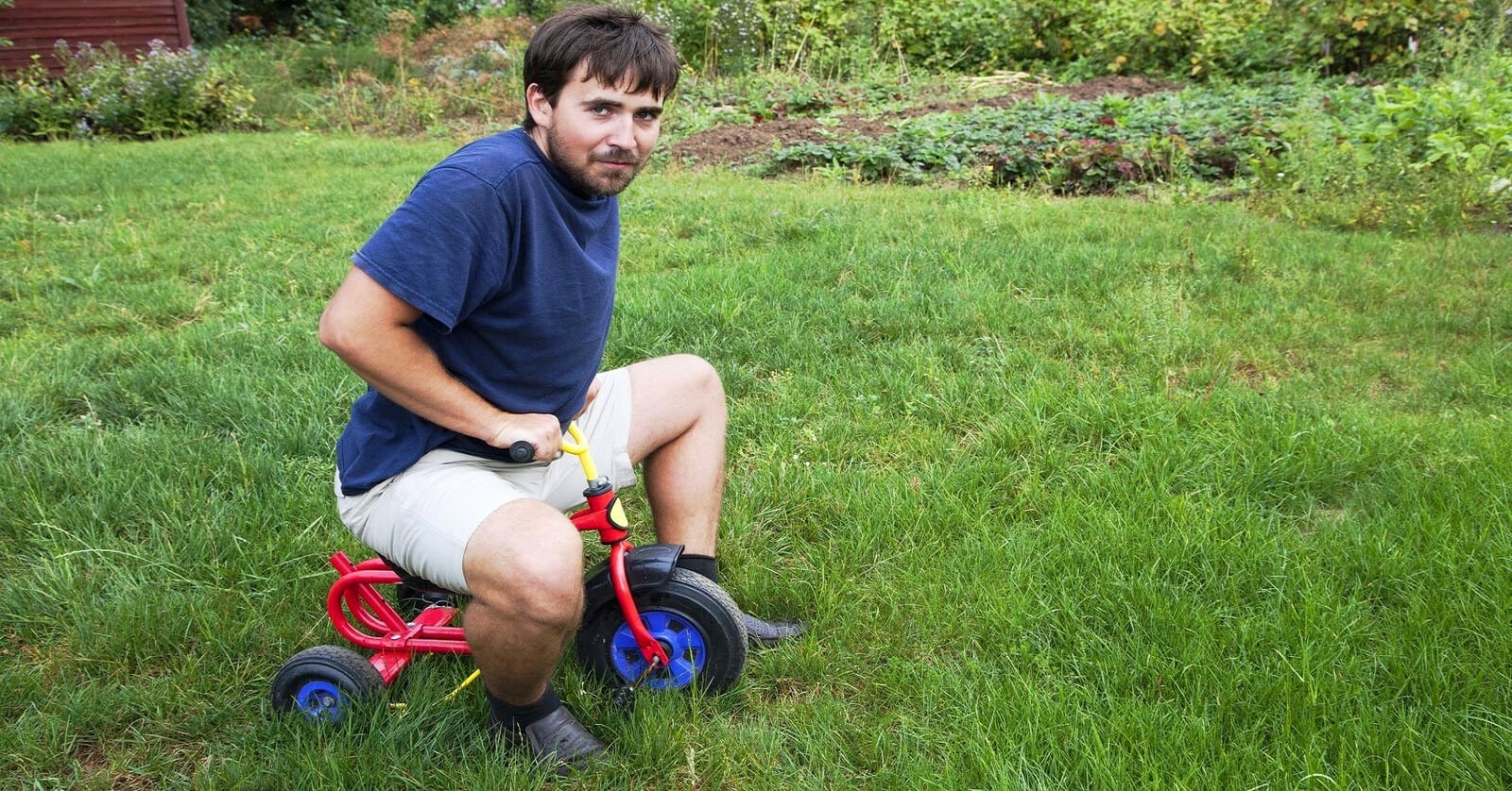 man trying to ride child's tricycle who needs to stop being childish