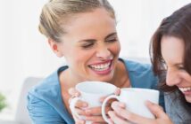 two women laughing and holding coffee in a home