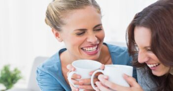 two women laughing and holding coffee in a home