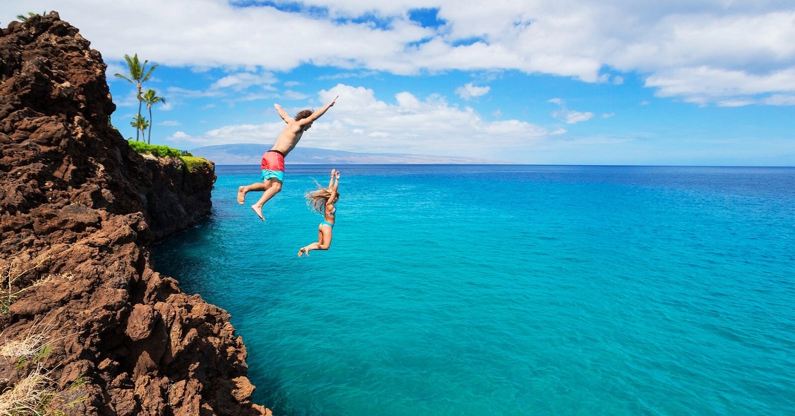 two young people taking a risk by jumping from cliffs into the ocean