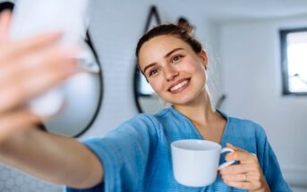 woman in a bath robe taking a selfie with a coffee in her hand