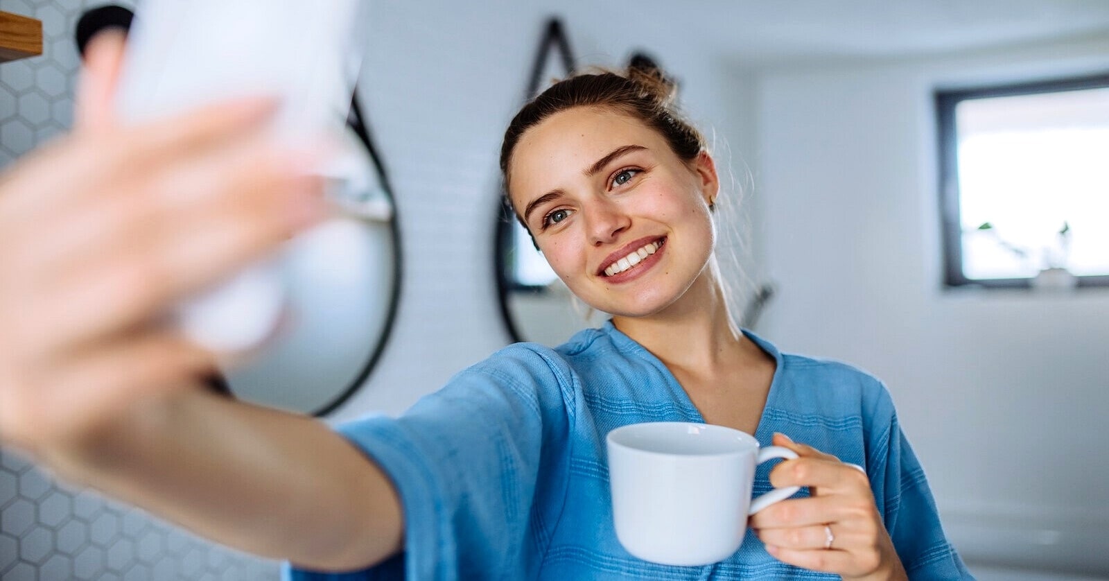 woman in a bath robe taking a selfie with a coffee in her hand