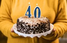 woman holding a cake with a four and zero candles on it to signify her 40th birthday