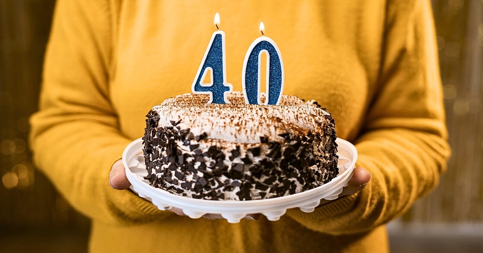 woman holding a cake with a four and zero candles on it to signify her 40th birthday