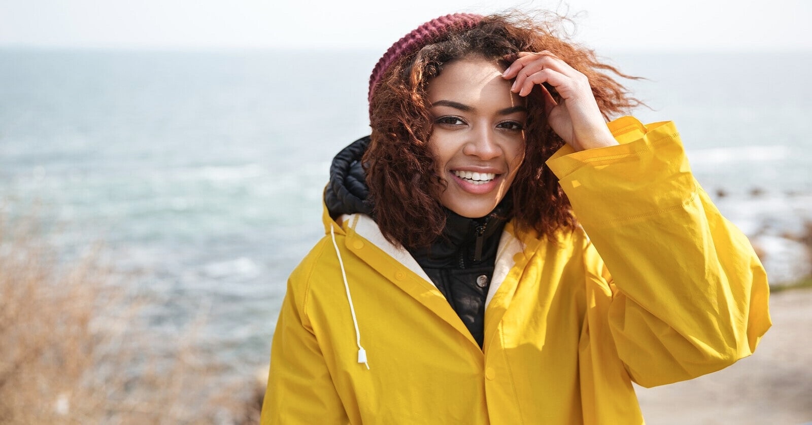 smiling woman wearing yellow raincoat with ocean in the background