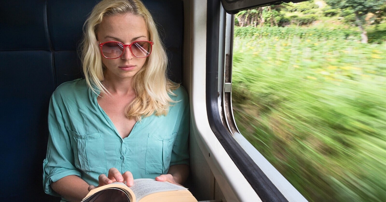 woman reading a book sitting by the window on a moving train