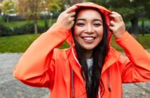 woman wearing a bright orange raincoat pulling the hood up over her head